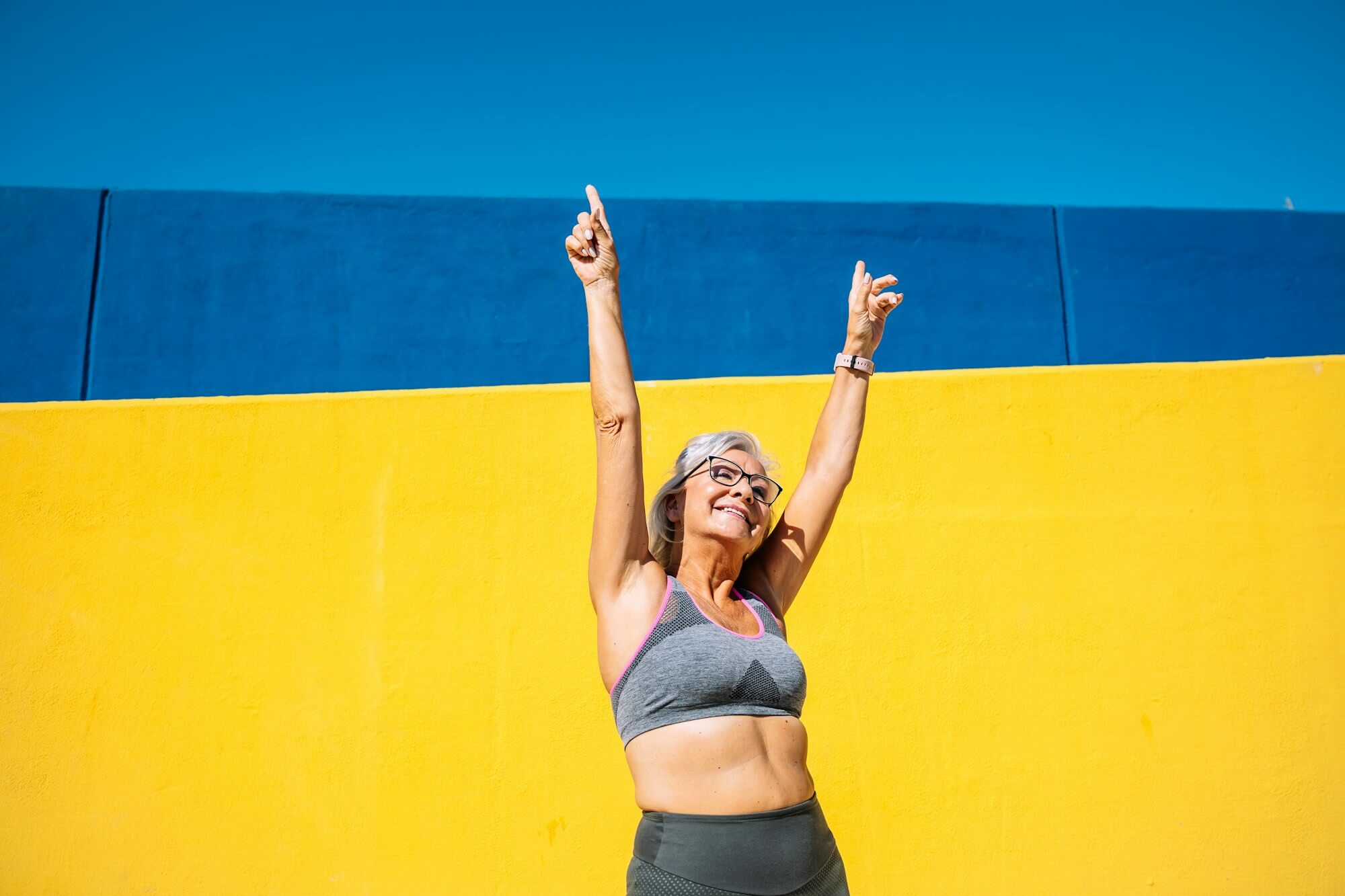 Joyful elder woman in sports clothes raising arms